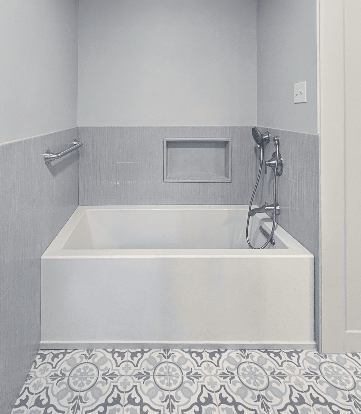 White soaking tub with gray tile surround and a patterned tile floor
