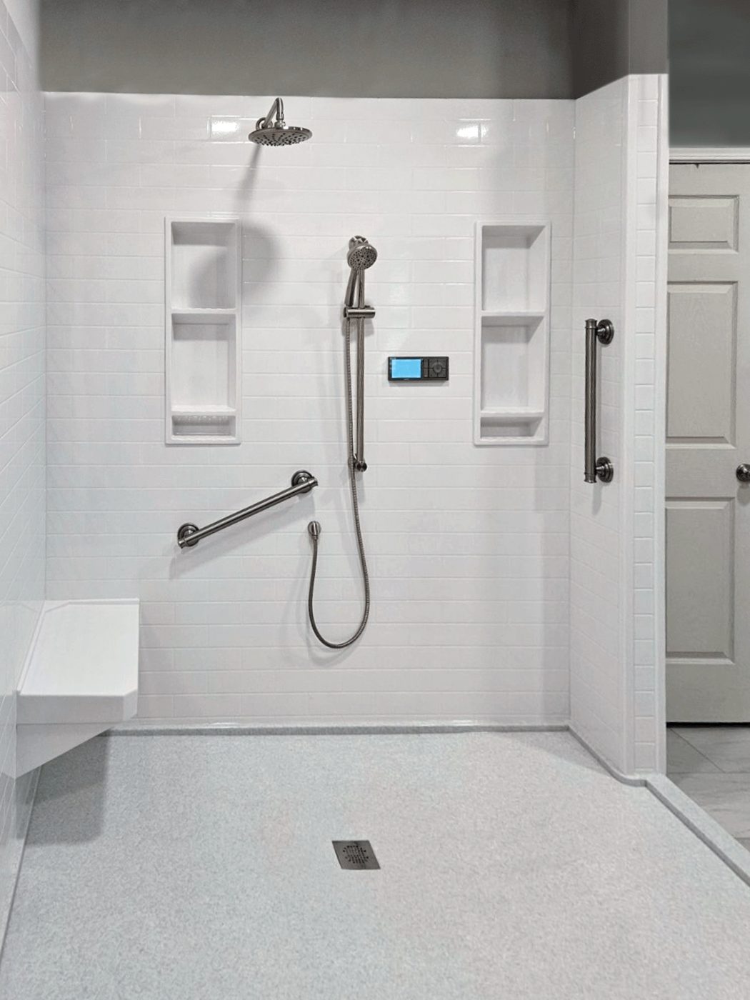 Easy-access white shower with a fold-down bench, grab bars, and a hand shower